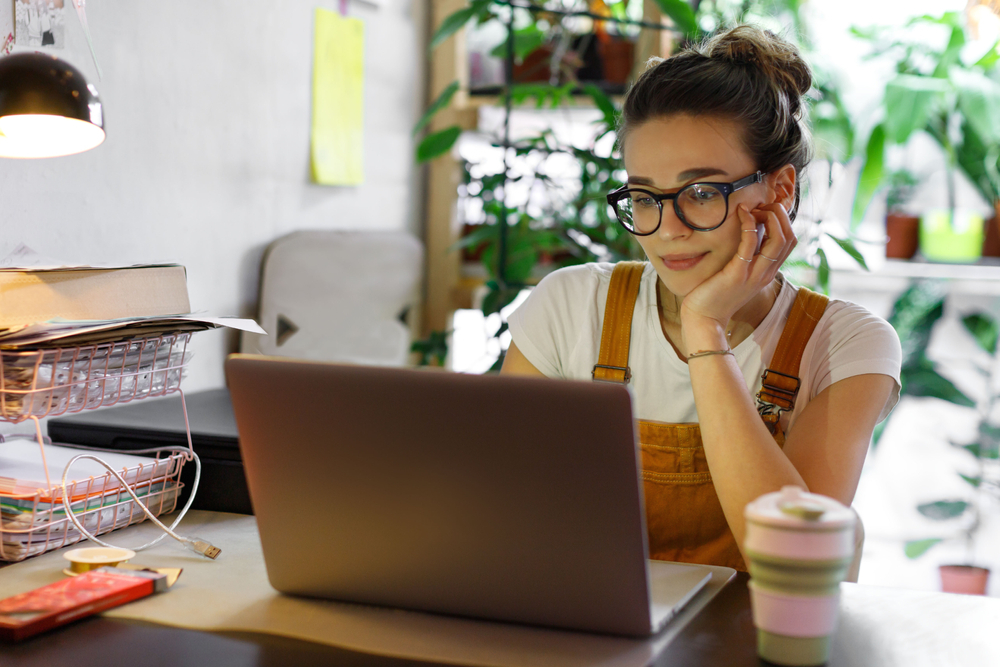 Remote work Vs. Traditional office: Young female in glasses using laptop to communicate with workers 